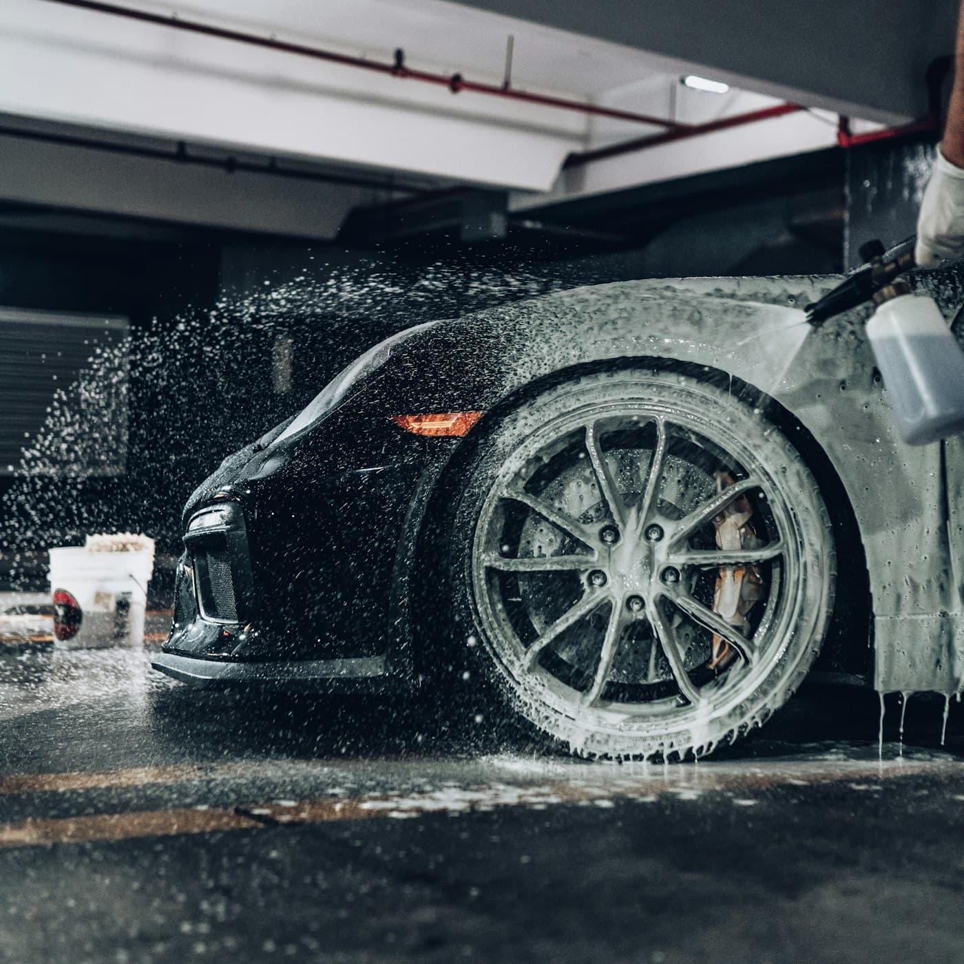 Foam covering a sports car and its wheel during a hand wash in a garage